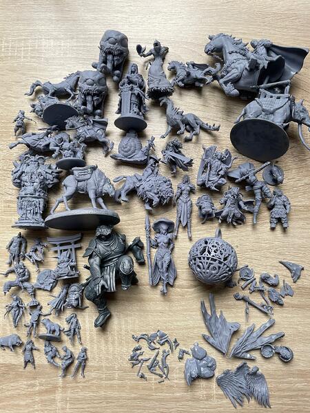 Uz koka virsmas izvietota liela neskrāsotu galda spēļu miniatūru kolekcija. (Captioned by AI)